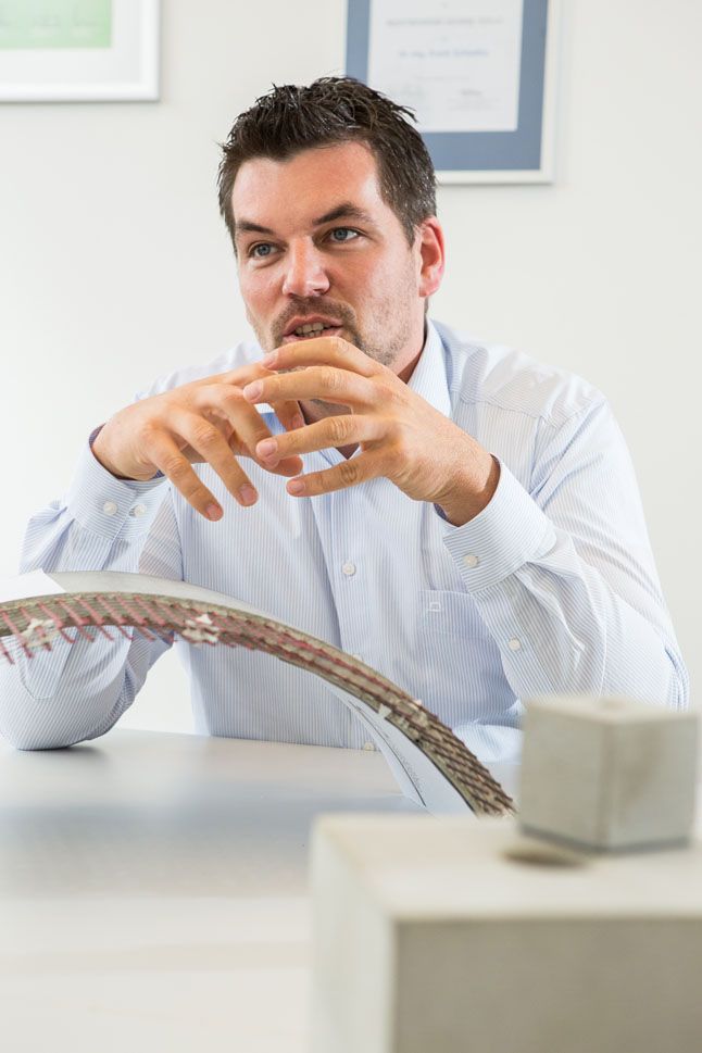 Bild zeigt einen Mann hinter einem bogenförmigen Modell an einem Schreibtisch sitzen