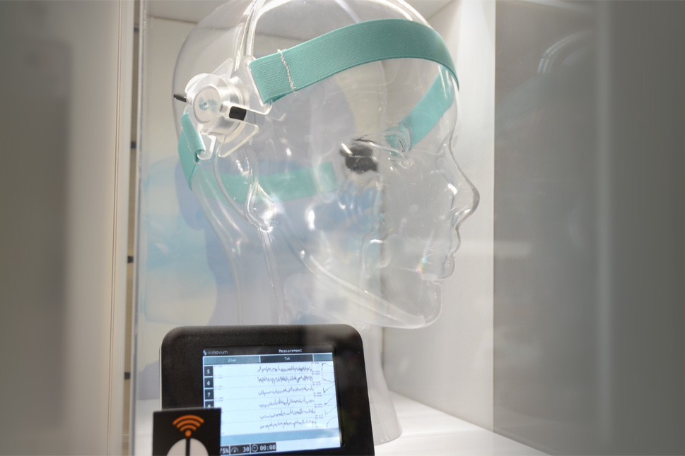 In einer Exponatsbox steht ein Modellkopf mit dem ACG-Gerät um seine Stirn und ein kleiner Monitor, der Gehirnströmungen darstellt.
