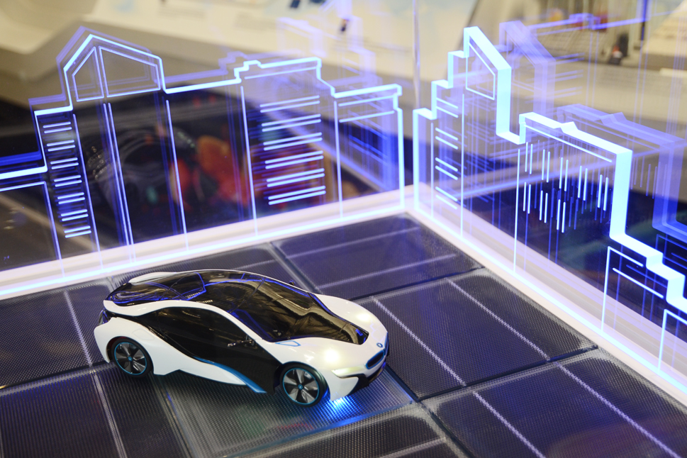 Bild der Exponatsbox: Ein kleines Modellauto auf einer PV-Oberfläche, eine futuristische, beleuchtete Stadt im Hintergrund.