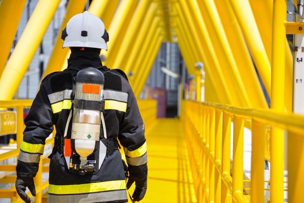 Bild zeigt einen Feuerwehrmann von hinten, der einen von gelben Metallstreben umrahmten Gang entlangläuft